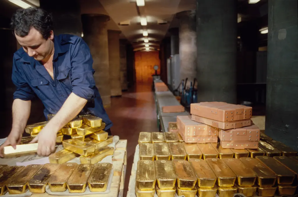 A man arranging gold bars in a vault alongside storage crates