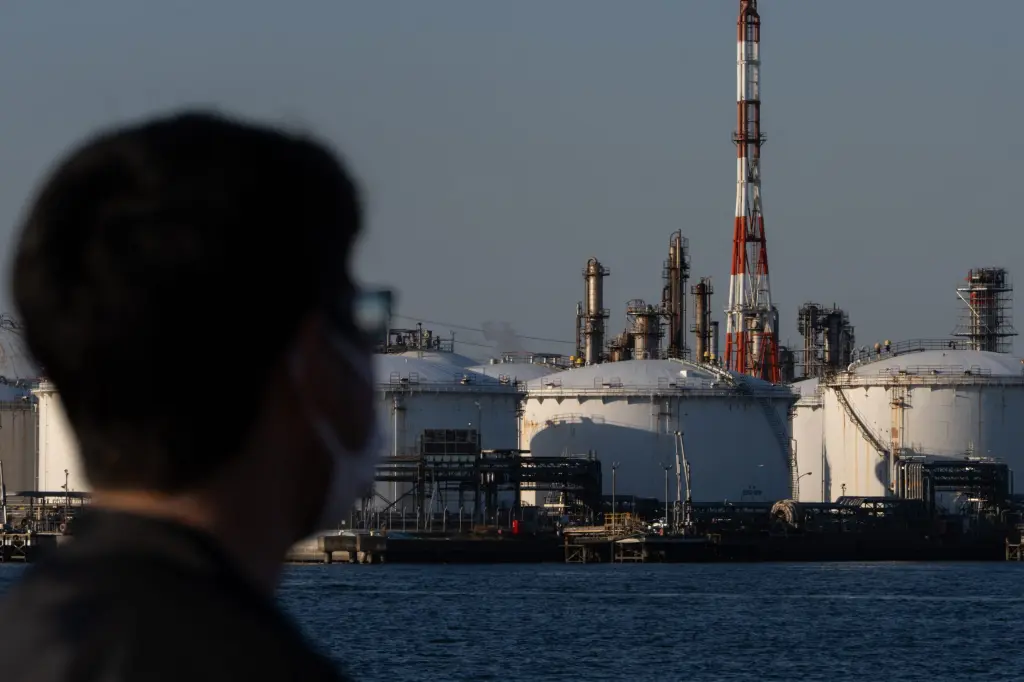 A man looking out at an oil refinery and storage tanks across the water