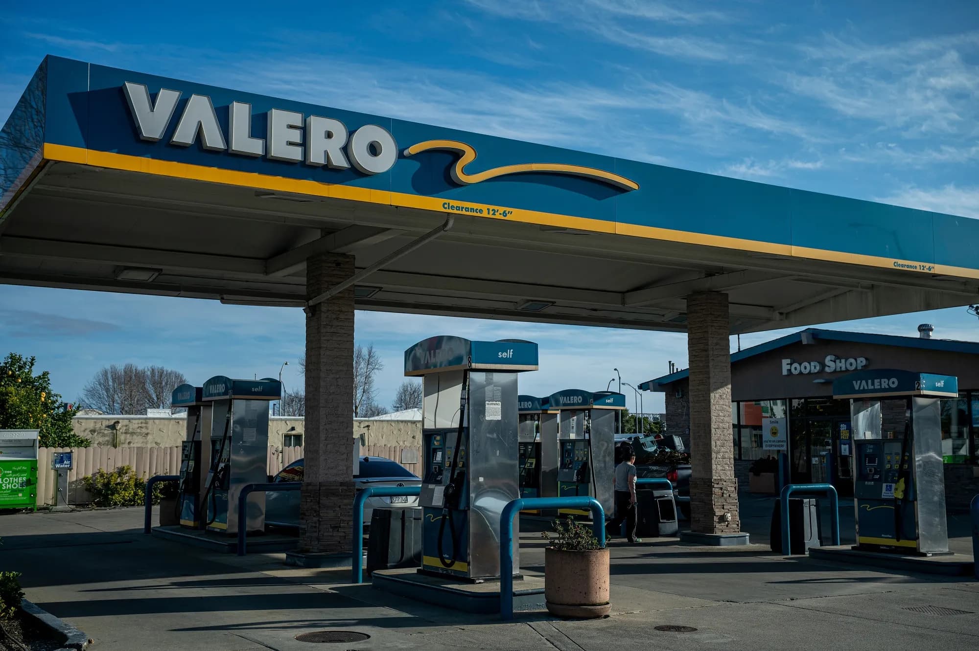 A Valero gas station sign and fuel pumps under a blue sky
